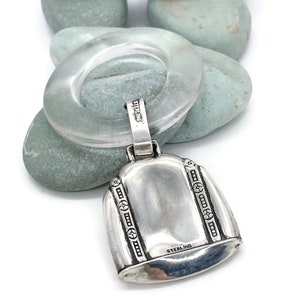 May include: A silver baby rattle with a clear plastic ring and a bell-shaped charm. The charm has a decorative design and the words "STERLING" engraved on the bottom.