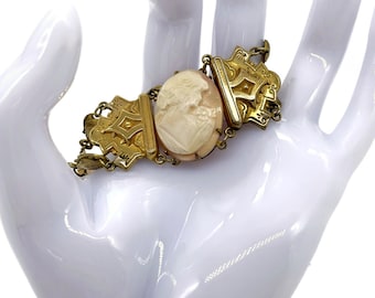 May include: A gold tone bracelet with a cameo featuring a carved profile of a woman. The bracelet has a hinged design with ornate details.