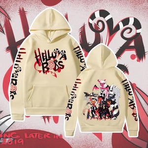 Puede incluir: Sudadera con capucha color crema con el texto "Helluva Boss" en negro y rojo en la parte delantera. Las mangas tienen texto adicional y la parte trasera muestra un grupo de personajes de dibujos animados. Una sudadera con capucha.