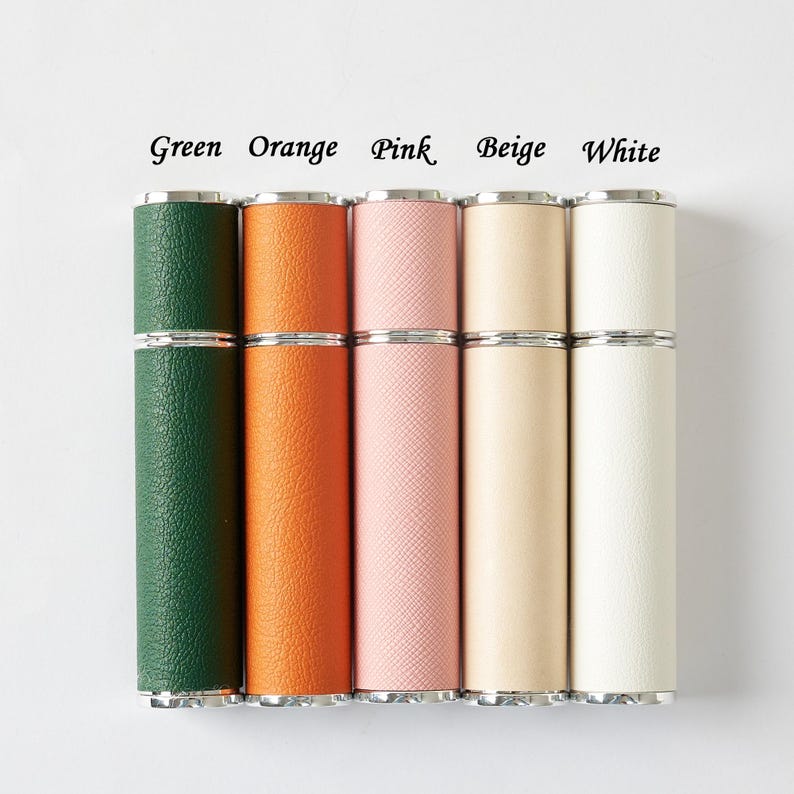 May include: A collection of five cylindrical perfume atomizers in various colors: green, orange, pink, beige, and white. Each atomizer has a silver-colored metal band at the top and bottom. The text "Green Orange Pink Beige White" is above the atomizers.