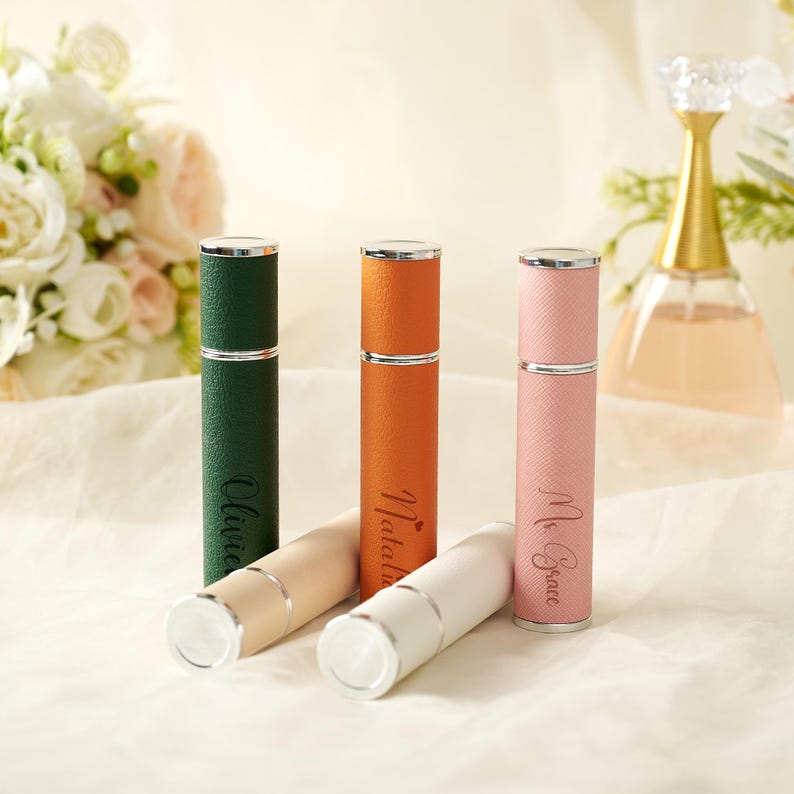 May include: Four personalized perfume atomizers in green, orange, pink, and white, with silver accents. Each atomizer is engraved with a name. The atomizers are cylindrical and have a textured leather-like appearance. A perfume bottle is in the background.