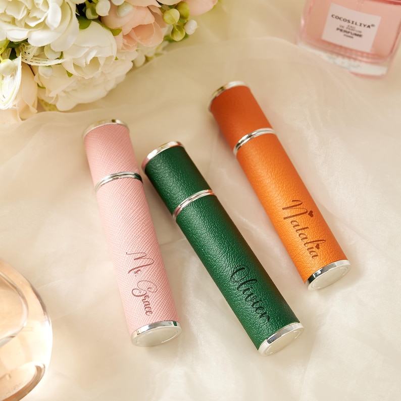 May include: Three personalized perfume atomizers in pink, green, and orange. Each atomizer has a silver band and a matching cap. The pink atomizer is engraved with "Mr. Grace", the green with "Oliver", and the orange with "Natalia".