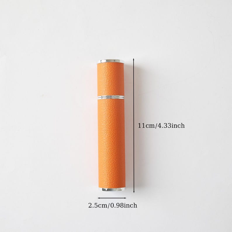 May include: An orange, cylindrical perfume atomizer with silver accents. The atomizer is 4.33 inches (11 cm) long and 0.98 inches (2.5 cm) in diameter. The surface has a textured, leather-like appearance. The image is set against a plain, light background.