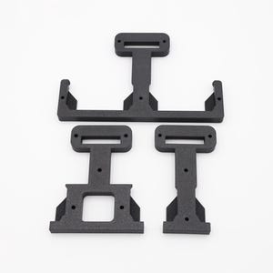 May include: Four black, geometric, 3D-printed components are arranged on a white background. The pieces include a large rectangular frame with two smaller T-shaped pieces and a larger T-shaped piece. The components have rectangular cutouts.