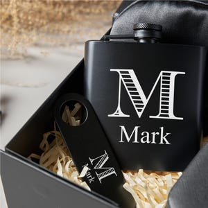 Peut inclure: Un ensemble de flasque et d'ouvre-bouteille noirs dans une bo&icirc;te cadeau. La flasque porte la lettre blanche "M" et le nom "Mark". L'ouvre-bouteille affiche &eacute;galement la lettre "M" et le nom "Mark". La bo&icirc;te contient du papier d&eacute;chiquet&eacute;.