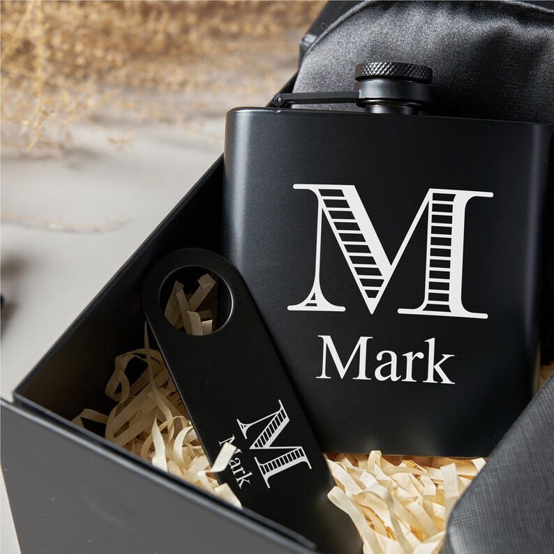 Peut inclure: Un ensemble de flasque et d'ouvre-bouteille noirs dans une bo&icirc;te cadeau. La flasque porte la lettre blanche "M" et le nom "Mark". L'ouvre-bouteille affiche &eacute;galement la lettre "M" et le nom "Mark". La bo&icirc;te contient du papier d&eacute;chiquet&eacute;.