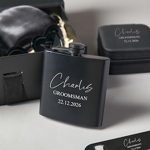Peut inclure: Une flasque noire personnalis&eacute;e avec le nom "Charles", le mot "Groomsman" et la date "22.12.2026" en &eacute;criture blanche. La flasque fait partie d'un coffret cadeau, comprenant une bo&icirc;te noire et d'autres accessoires. Id&eacute;al pour un mariage.