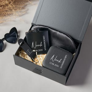 Peut inclure: Coffret cadeau noir contenant une flasque, un masque pour les yeux, un miroir compact et un ouvre-bouteille. Chaque article est personnalis&eacute; avec le nom "Noah" et une date. Lunettes de soleil en forme de c&oelig;ur visibles.