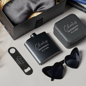 Peut inclure: Un coffret cadeau noir comprenant une flasque, des lunettes de soleil en forme de c&oelig;ur, un ouvre-bouteille, un &eacute;tui &agrave; montre et un masque pour les yeux. La flasque, l'ouvre-bouteille et l'&eacute;tui &agrave; montre sont grav&eacute;s du nom "Charles" et du texte "Groomsman 22.12.2026".