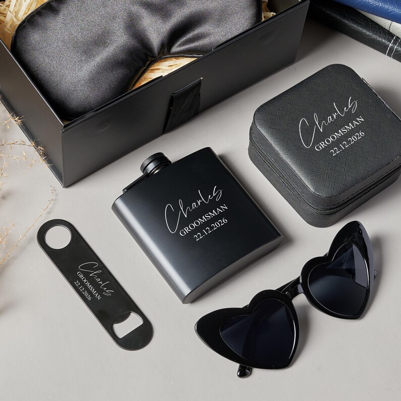 Peut inclure: Un coffret cadeau noir comprenant une flasque, des lunettes de soleil en forme de c&oelig;ur, un ouvre-bouteille, un &eacute;tui &agrave; montre et un masque pour les yeux. La flasque, l'ouvre-bouteille et l'&eacute;tui &agrave; montre sont grav&eacute;s du nom "Charles" et du texte "Groomsman 22.12.2026".