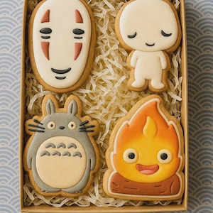 Puede incluir: Una caja con cuatro galletas decoradas con personajes de Studio Ghibli. Las galletas incluyen a Sin Rostro, un Kodama, Totoro y Calcifer. Est&aacute;n decoradas con glaseado y descansan sobre papel triturado.