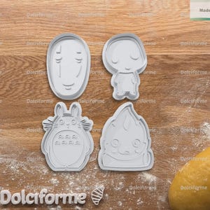 Puede incluir: Cuatro cortadores de galletas grises de varias formas est&aacute;n sobre una superficie de madera espolvoreada con harina. Los cortadores incluyen una cara, una figura peque&ntilde;a, un personaje tipo Totoro y una criatura estilizada. Una bola de masa est&aacute; a la derecha. El texto "Made in Italy" es visible.