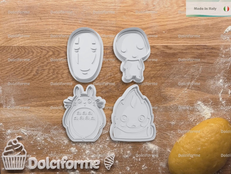 Puede incluir: Cuatro cortadores de galletas grises de varias formas est&aacute;n sobre una superficie de madera espolvoreada con harina. Los cortadores incluyen una cara, una figura peque&ntilde;a, un personaje tipo Totoro y una criatura estilizada. Una bola de masa est&aacute; a la derecha. El texto "Made in Italy" es visible.