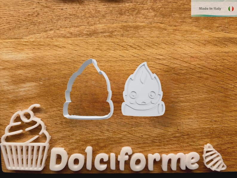 Puede incluir: Cortadores de galletas de pl&aacute;stico blanco con forma de cupcake, un personaje en forma de llama y una llama estilizada. La palabra "Dolciforme" est&aacute; escrita con letras blancas. El fondo es una superficie de madera.