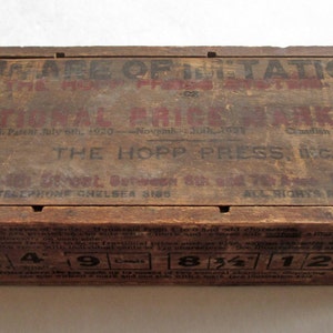 May include: A vintage wooden box with printed text in red and black. The text includes "BEWARE OF IMITATIONS" and "NATIONAL PRICE MARKING". The box has measurements printed on the bottom and is likely an antique.