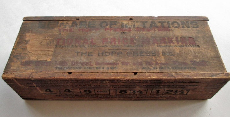 May include: A vintage wooden box with printed text in red and black. The text includes "BEWARE OF IMITATIONS" and "NATIONAL PRICE MARKING". The box has measurements printed on the bottom and is likely an antique.