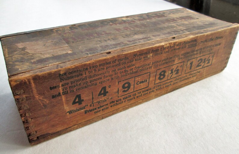 May include: A vintage wooden box with printed text and numerals. The box is a warm brown color, showing signs of age and wear. The text includes prices like 4&cent;, 9&cent;, 8 1/2&cent;, and 1 1/2&cent;. The box is likely for storing cards.