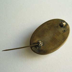 May include: An antique oval brooch with a pin closure. The brooch has a bronze-colored metal finish and a simple design. The pin is long and slender, and the clasp is a simple, functional design. The brooch is likely vintage.