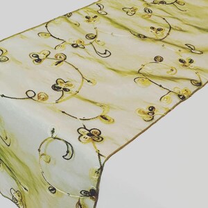 May include: A sheer ivory table runner with an embroidered floral design in shades of gold and brown. The runner features delicate vines and flowers, creating a romantic and elegant look.