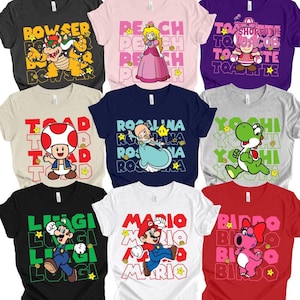 May include: Collection of graphic t-shirts featuring characters from the Super Mario video game series. Designs include Bowser, Peach, Toad, Rosalina, Yoshi, Luigi, Mario, and Birdo. Each shirt has the character's name and a star graphic.