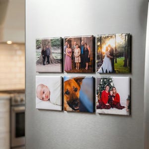 May include: Six square canvas prints with family photos are displayed on a refrigerator. The images include a baby, a dog, a couple, a wedding, and a family portrait. The prints are arranged in two rows of three.