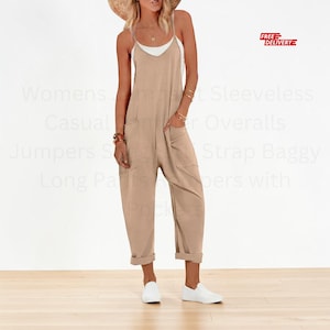 May include: A beige sleeveless jumpsuit featuring a V-neckline, thin shoulder straps, and two large patch pockets on the front. The garment has a loose, baggy fit with cropped trouser legs that are cuffed at the bottom, worn over a white vest top.