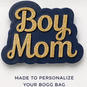 May include: A navy blue and gold "Boy Mom" accessory. The text is in a gold, textured font, set against a navy blue background with a scalloped edge. The bottom text reads "MADE TO PERSONALIZE YOUR BOGG BAG".