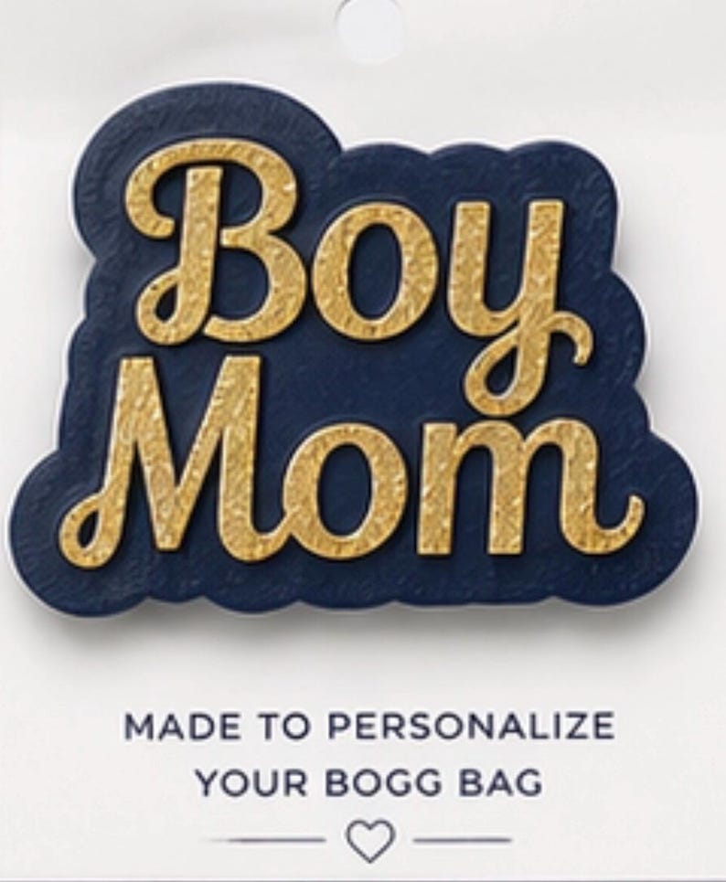 May include: A navy blue and gold "Boy Mom" accessory. The text is in a gold, textured font, set against a navy blue background with a scalloped edge. The bottom text reads "MADE TO PERSONALIZE YOUR BOGG BAG".