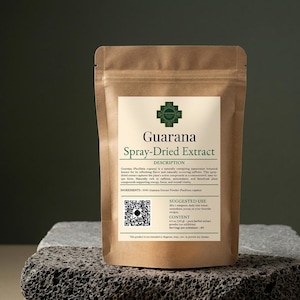 Pode incluir: Um saco de papel castanho de Extrato de Guarana Spray-Dried, com um rótulo branco com texto e um logótipo verde. O rótulo inclui a descrição, os ingredientes e o uso sugerido. O saco está sobre uma superfície cinzenta texturizada.