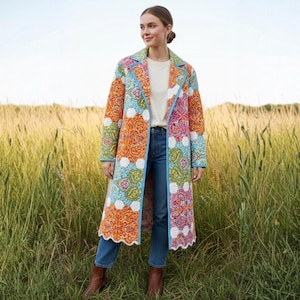 Pu&ograve; includere: Un cappotto lungo trapuntato con un colorato motivo paisley in arancione, blu, rosa e verde. Il cappotto ha un bordo azzurro e un orlo smerlato. La persona indossa jeans blu e stivali marroni.