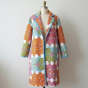Pu&ograve; includere: Un cappotto trapuntato colorato con un vivace motivo paisley in arancione, rosa, blu e verde. Il cappotto ha un bordo blu chiaro e un orlo smerlato. Il cappotto &egrave; esposto su un manichino.