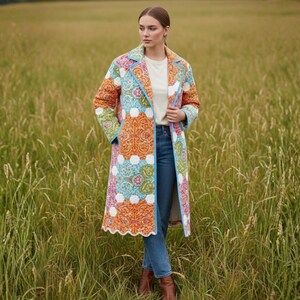 Pu&ograve; includere: Un lungo cappotto patchwork colorato con un motivo floreale nei toni dell'arancione, blu, bianco e verde. Il cappotto ha un bordo azzurro e un orlo smerlato. Il cappotto &egrave; indossato all'aperto in un campo di erba alta.