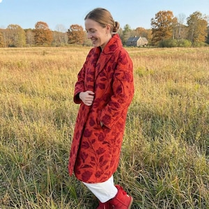 May include: A long, quilted coat in a vibrant red hue, adorned with a floral pattern in a deeper shade of red. The coat features a shawl collar and pockets, offering a stylish and warm outerwear option.