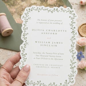 Puede incluir: Una tarjeta de invitaci&oacute;n de boda blanca con borde festoneado y un borde de enredadera bot&aacute;nica verde. El texto dice: The honour of your presence is requested at the wedding of Olivia Charlotte Ashford and William James Sinclair, 21 de junio de 2027.