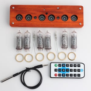 May include: A wooden clock base with six circular display openings, accompanied by vacuum tubes, brass rings, a remote control, and a cable. The clock's wooden base is a warm brown color.