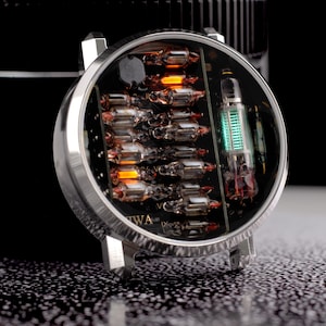 May include: A round wristwatch case featuring a nixie tube display with multiple small glass vacuum tubes arranged in a grid. The tubes emit a warm orange glow, while a larger vertical tube on the right side displays a bright green light.