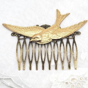 May include: A vintage-style hair comb featuring a gold-colored bird in flight. The bird is intricately detailed with outstretched wings, perched atop a comb with multiple tines. The comb has an antique brass finish, adding to its classic appeal.