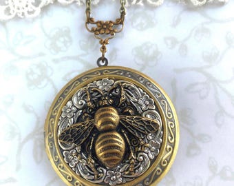 May include: A vintage-style round locket necklace with a detailed bee design. The locket features a gold-tone frame with silver accents and a floral border. The bee is intricately detailed, and the necklace has a delicate chain.