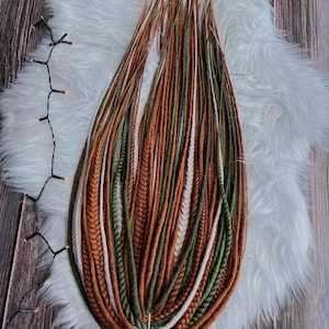 May include: A collection of synthetic hair extensions featuring a mix of long, thin dreadlocks and braided strands in earthy tones of rust orange, forest green, and cream white, all gathered together at the base with a simple white string tie.