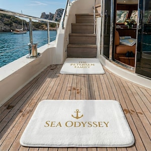 May include: Two white rectangular floor mats placed on a wooden boat deck. The bottom mat features a gold anchor icon and the text SEA ODYSSEY. The top mat, positioned near the stairs, displays the text THE PETERSEN FAMILY in gold lettering.