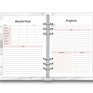 May include: Open white planner with sections for Month/Year and Projects. The planner is open to a double-page spread with lined pages and pink accents. A white pen rests on the left side.