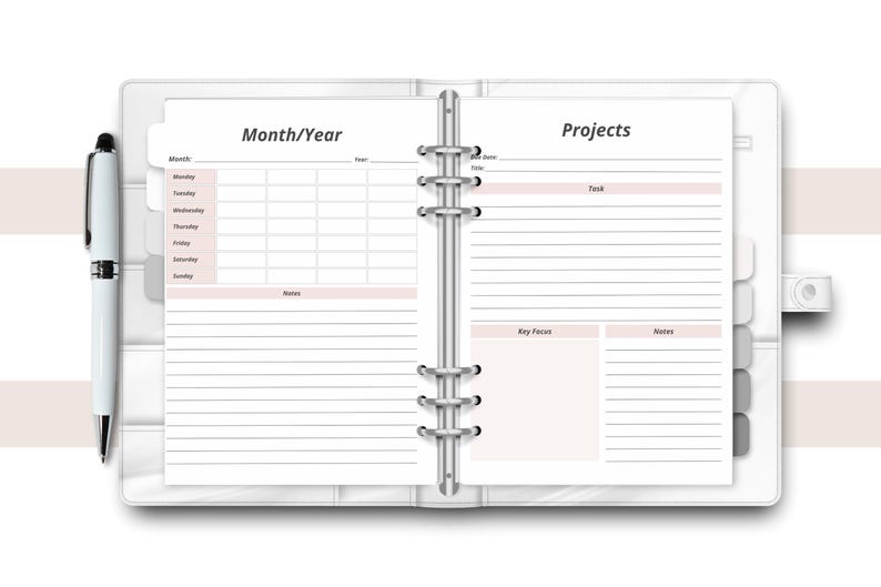 May include: Open white planner with sections for Month/Year and Projects. The planner is open to a double-page spread with lined pages and pink accents. A white pen rests on the left side.