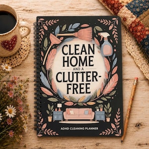 May include: A black spiral-bound planner titled CLEAN HOME AND A CLUTTER-FREE ADHD CLEANING PLANNER. The cover features a central illustration of a living room with a sofa, surrounded by a wreath of colourful leaves, a broom, and a spray bottle.