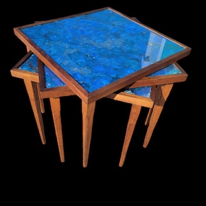 May include: Three nesting tables with blue resin tops and dark wood legs. The tops are a mottled blue with a marbled effect.