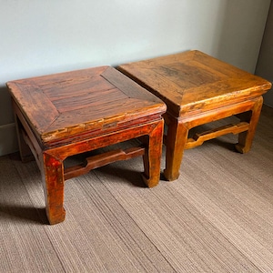 May include: Two antique wooden square stools. One stool is stained a deep red, the other a light brown. Both have a square top and a decorative apron. The stools are approximately 18 inches wide and 18 inches deep.