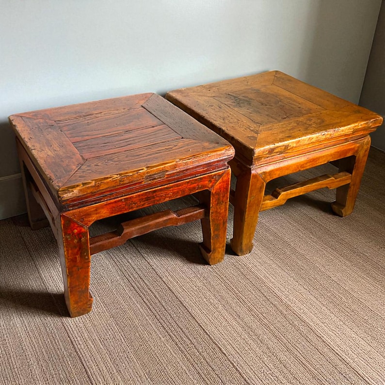 May include: Two antique wooden square stools. One stool is stained a deep red, the other a light brown. Both have a square top and a decorative apron. The stools are approximately 18 inches wide and 18 inches deep.