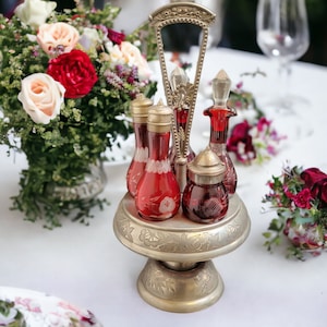May include: A vintage silver-plated condiment set with red glass bottles and a decorative base. The set is on a white tablecloth with floral arrangements.