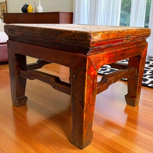 May include: A rectangular, antique wooden table with a dark reddish-brown finish. The table has a thick top and sturdy, carved legs. The wood shows signs of age and wear, adding to its vintage appeal. The table is approximately 24 inches long, 24 inches wide, and 18 inches high.
