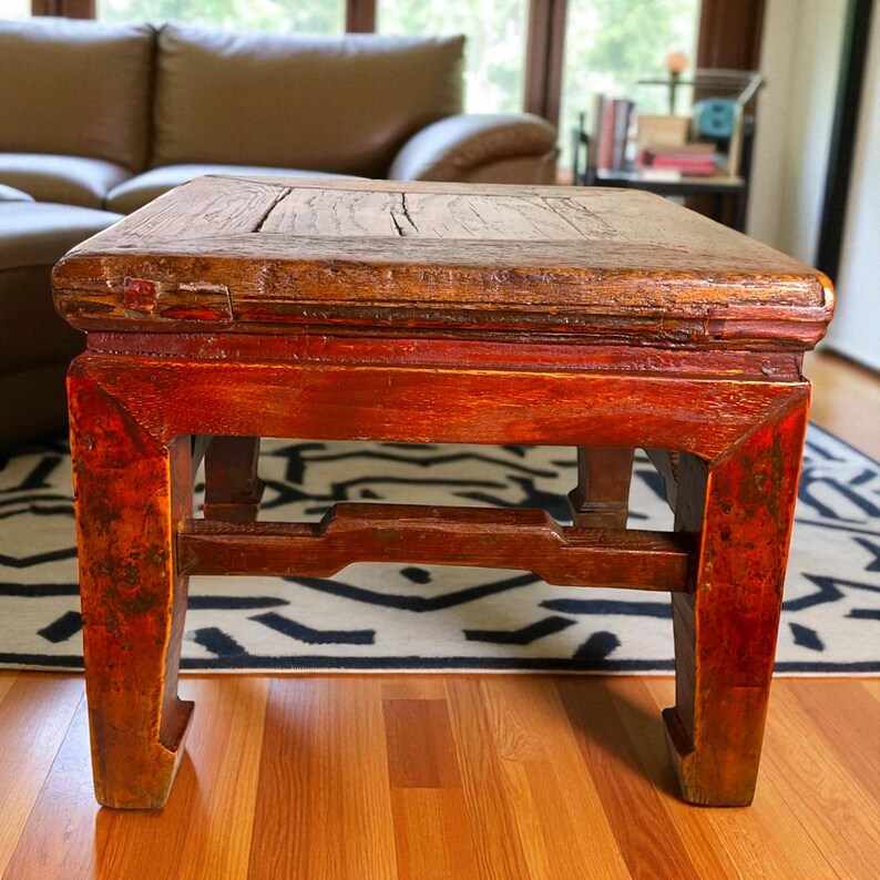May include: A square, antique wooden table with a distressed finish. The tabletop is a warm brown, while the legs and frame are a vibrant red-orange. The table has a sturdy, traditional design, perfect for a living room or entryway.