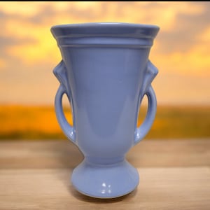 May include: A light blue ceramic vase with two handles. The vase has a classic, elegant design and is perfect for displaying flowers.